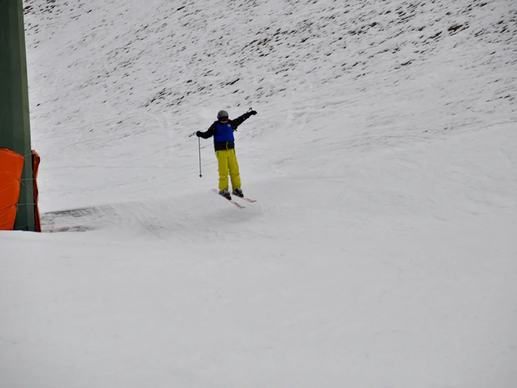 Skifahrer in gelber Hose fährt mit ausgebreiteten Armen bergab.